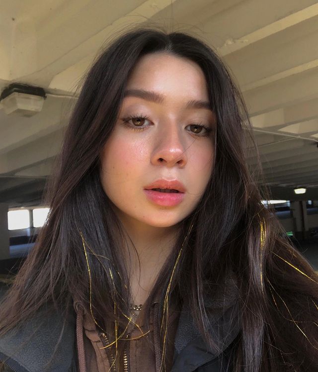 cabelo-com-fios-de-ouro Selfie de uma mulher. Ela está com uma maquiagem natural e cabelo liso solto com detalhe de fios de ouro. Ela olha para a câmera e não sorri.