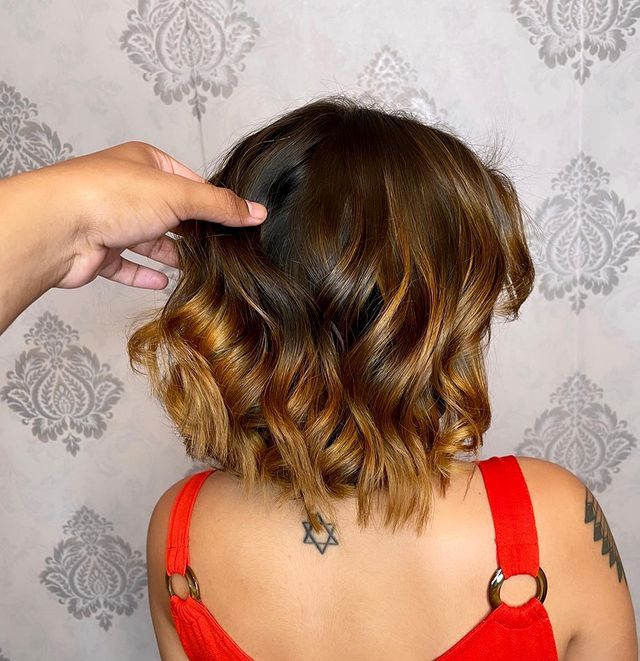cabelo-curto-iluminado Foto de uma mulher de costas. Ela usa uma blusa laranja e está com o cabelo curto solto com a técnica de moreno iluminado.