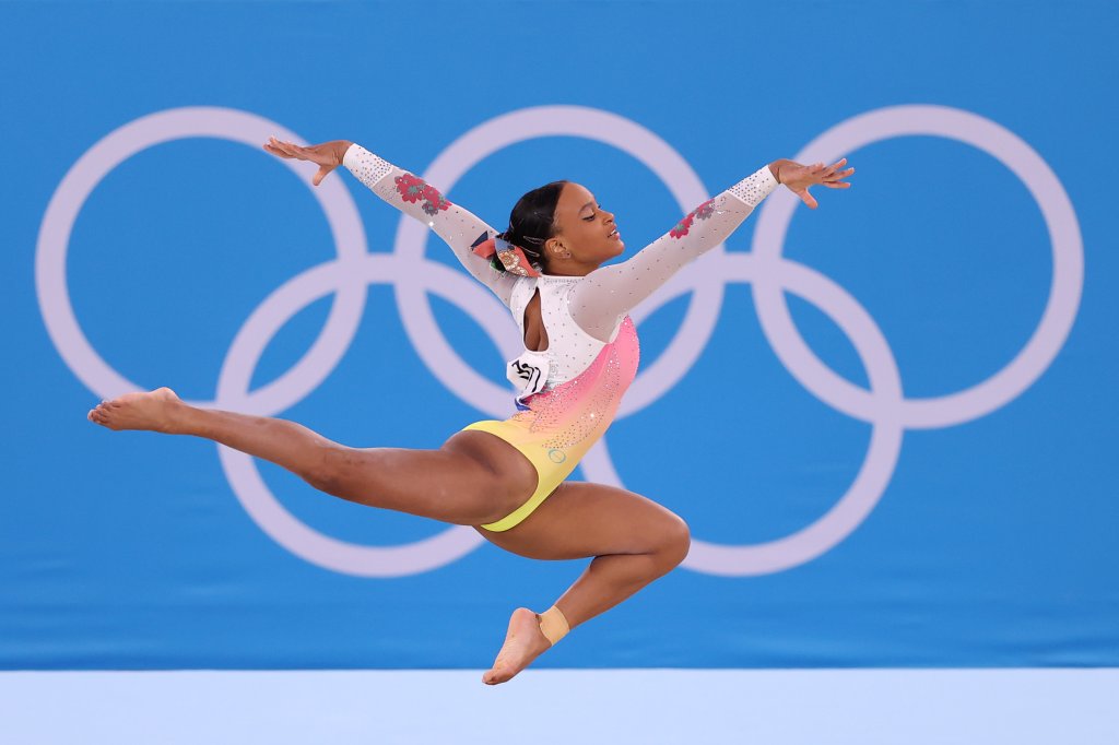 A ginasta Rebeca Andrade competindo nas Olimpíadas de Tóquio usando collant branco, rosa e amarelo