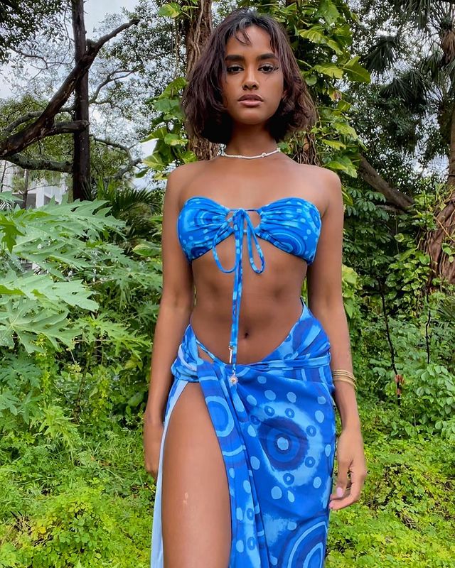 conjunto-de-biquini-azul Foto de uma mulher em um ambiente com árvores e gramado. Ela usa um biquíni azul estampado com saia longa com a mesma estampa. Ela olha para a câmera e não sorri.