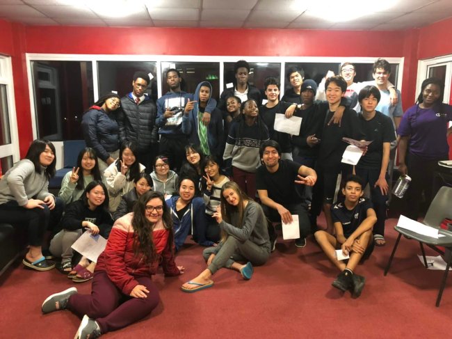 Como é morar em um internato no interior da Inglaterra? Foto de Marine, da Galera CH, no intercâmbio. Ela está numa sala vermelha e posa ao lado dos colegas de classe com diplomas na mão