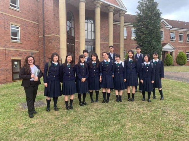 Foto de Marine, da Galera CH, em seu primeiro dia de aula no intercâmbio. Ela está de calça e terninho preto, e posa ao lado dos colegas de sala