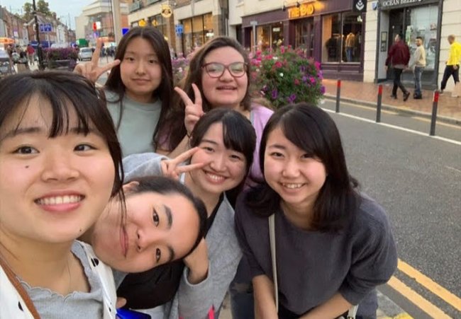 Como é morar em um internato no interior da Inglaterra? Foto de Marine, da Galera CH, durante intercâmbio. Ela tira uma selfie na rua com as amigas, durante passeio. Todas são asiáticas, menos a Marine, que é branca
