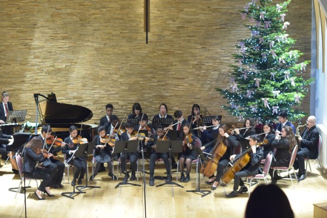 Como é morar em um internato no interior da Inglaterra? Foto de Marine, da Galera CH, durante intercâmbio. Ela se apresenta com a orquestra do colégio na festa de sinal de ano. Tem uma árvore de Natal enorme atrás dos instrumentistas