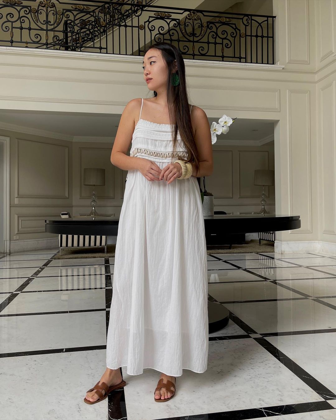 look-vestido-branco-giuliasong Garota usando vestido branco longo com rasteirinha marrom e olhando para o lado com as duas mãos na frente do corpo