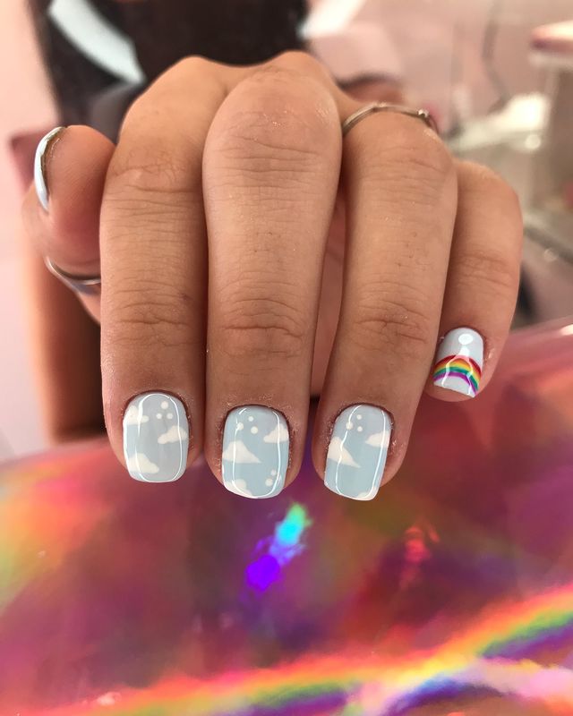 unha-azul-decorada-com-nuvens Foto de uma mão com as unhas com esmalte azul e decoração de nuvens brancas.