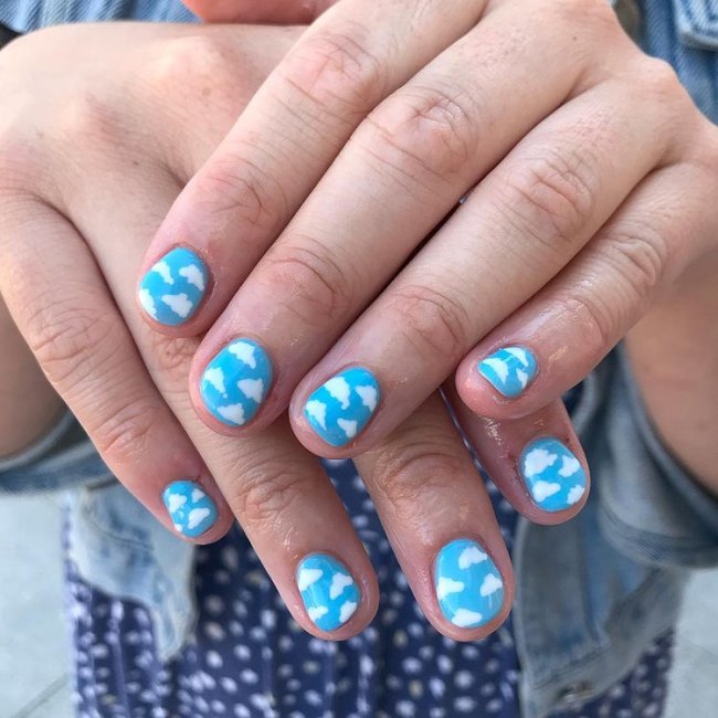 unhas com decoração de nuvens Fotos de mãos com as unhas decoradas com esmalte azul e decoração de nuvens brancas.