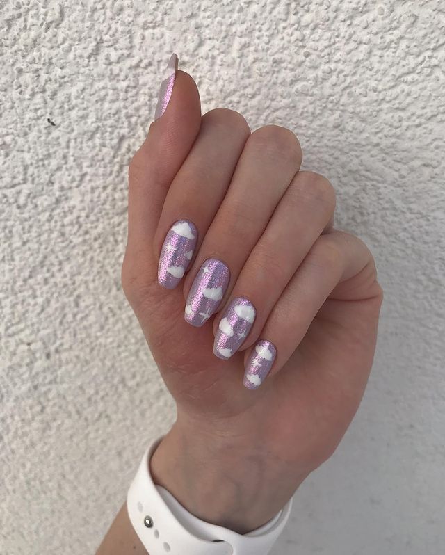 unhas-holograficas-decoradas-com-nuvens Foto de uma mão com unhas holográficas com decoração de nuvens brancas.