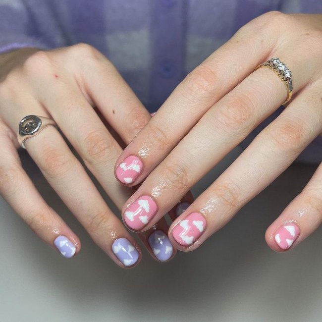 unhas-lilas-rosa-com-nuvens Foto de mãos com esmalte lilás e rosa com desenho de nuvens lilás.