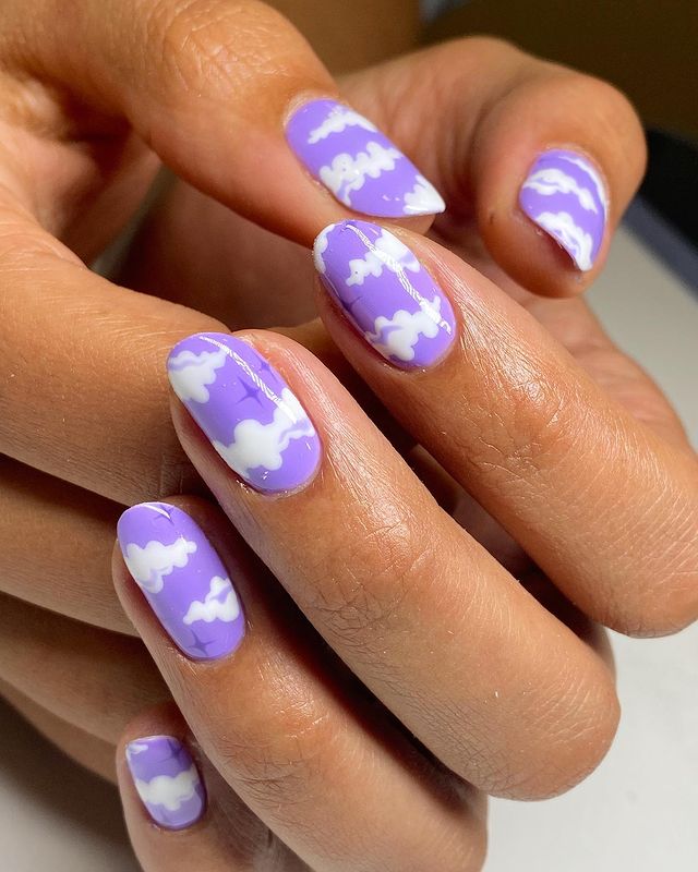 unhas-roxas-com-decoracao-de-nuvens Foto de unhas roxas com decoração de nuvens brancas.