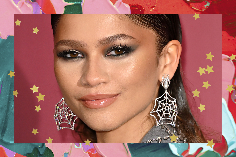 Zendaya na photocall de Homem-Aranha: Sem Volta para Casa, em Londres usando brincos que imitam teia de aranha e maquiagem com sombra preta esfumada. A montagem possui fundo com tintas em verde, vermelho e rosa e estrelinhas douradas