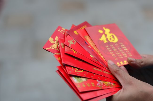 Horóscopo Chinês: confira as previsões para 2022, o Ano do Tigre de Água Uma mão segurando várias cartas vermelhas com escritos em chinês na cor dourado