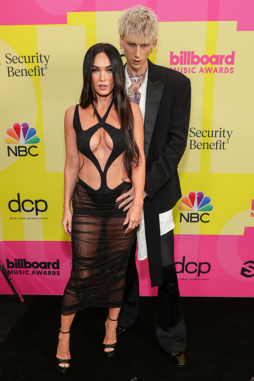 Megan Fox e Machine Gun Kelly posando para foto em carpet; os dois estão com expressões sérias