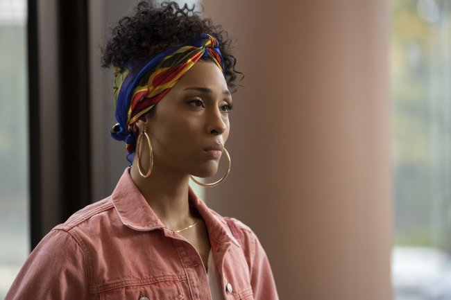 Imagem de MJ Rodriguez na série Pose. Ela tem o cabelo cacheado preso em um coque alto e usa um lenço. A jaqueta é rosa e ela está com cara de preocupação