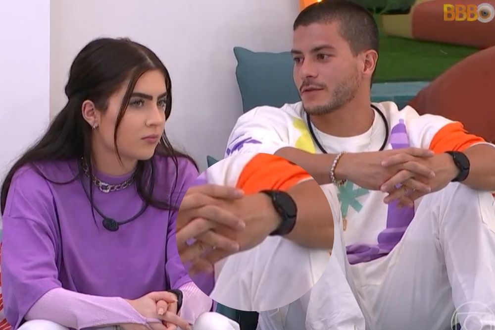 Jade Picon e Arthur Aguiar sentados lado a lado na área externa do BBB22; um círculo destacando o relógio preto no pulso do brother está centralizado na imagem