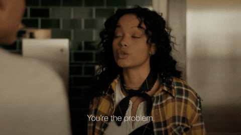 cabelo-cacheado-gossip-girl GIF de cena do reboot de Gossip Girl da HBO Max. Na cena a personagem Zoya usa um casaco xadrez, camisa branca e lenço preto no pescoço. Ela está com o cabelo cacheado solto, olha para frente e fala