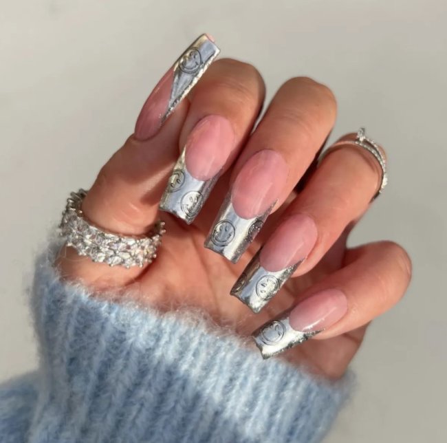 francesinha metalizada Foto de uma mão com as unhas longas e francesinha metalizada com detalhe de rostinhos felizes.