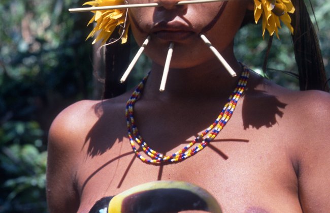 Close de uma garota yanomami segurando um tucano. Só dá para ver o nariz dela e a boca. 