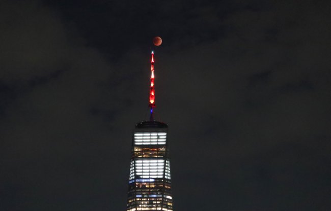 Lua de Sangue pelo mundo: veja fotos do eclipse lunar total desta segunda (16) Foto da Lua de Sangue brilhando avermelhada atrás de um prédio enorme