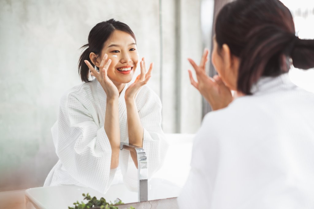 Garota coreana fazendo skincare e sorrindo em frente ao espelho