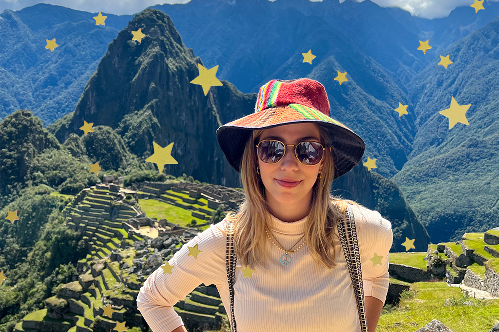 A repórter Sofia Duarte usando chapéu colorido, óculos de sol, blusa bege em frente a Machu Picchu, no Peru