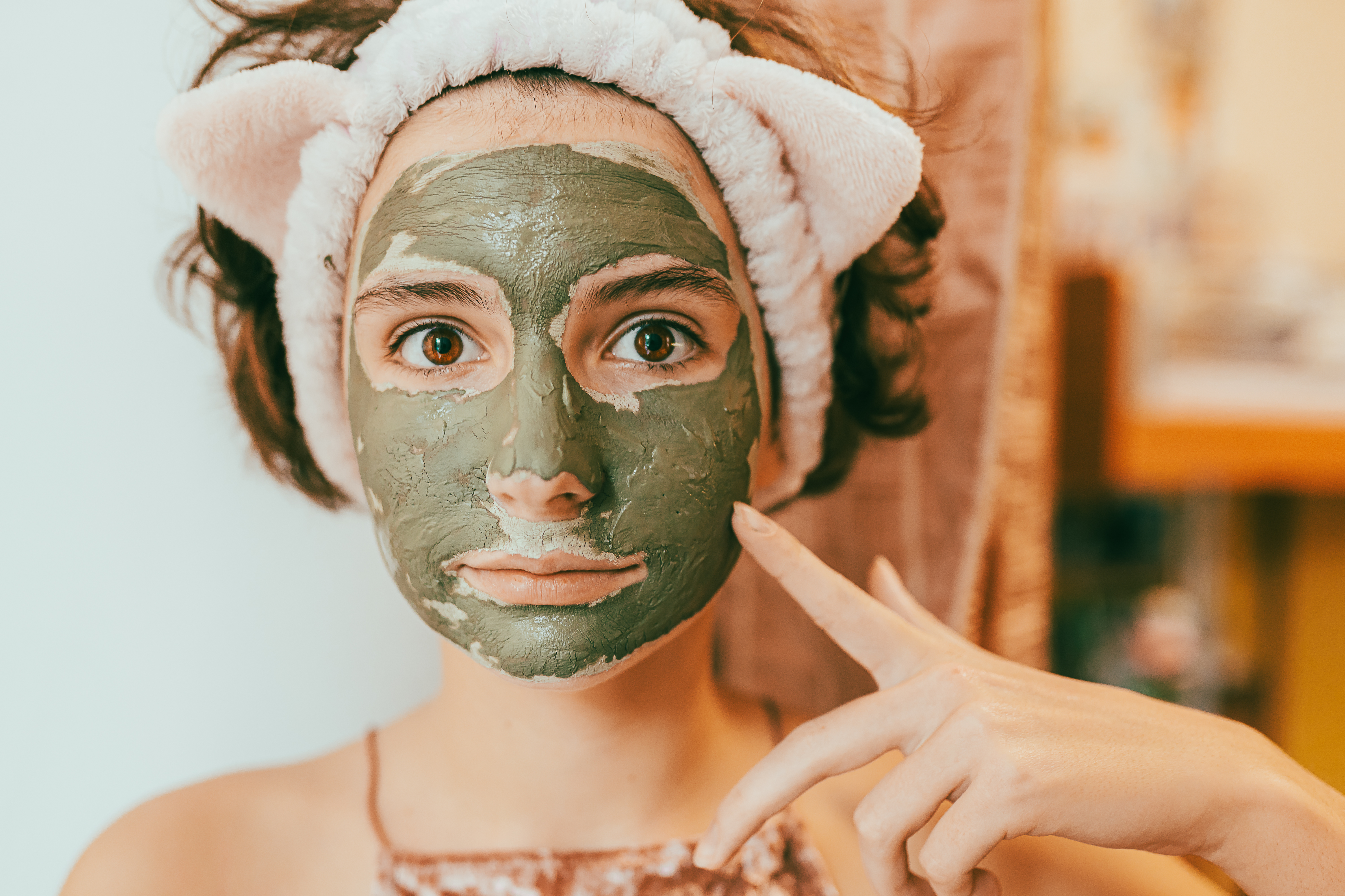 Garota com máscara facial de argila verde, expressão facial séria e uma faixa no cabelo