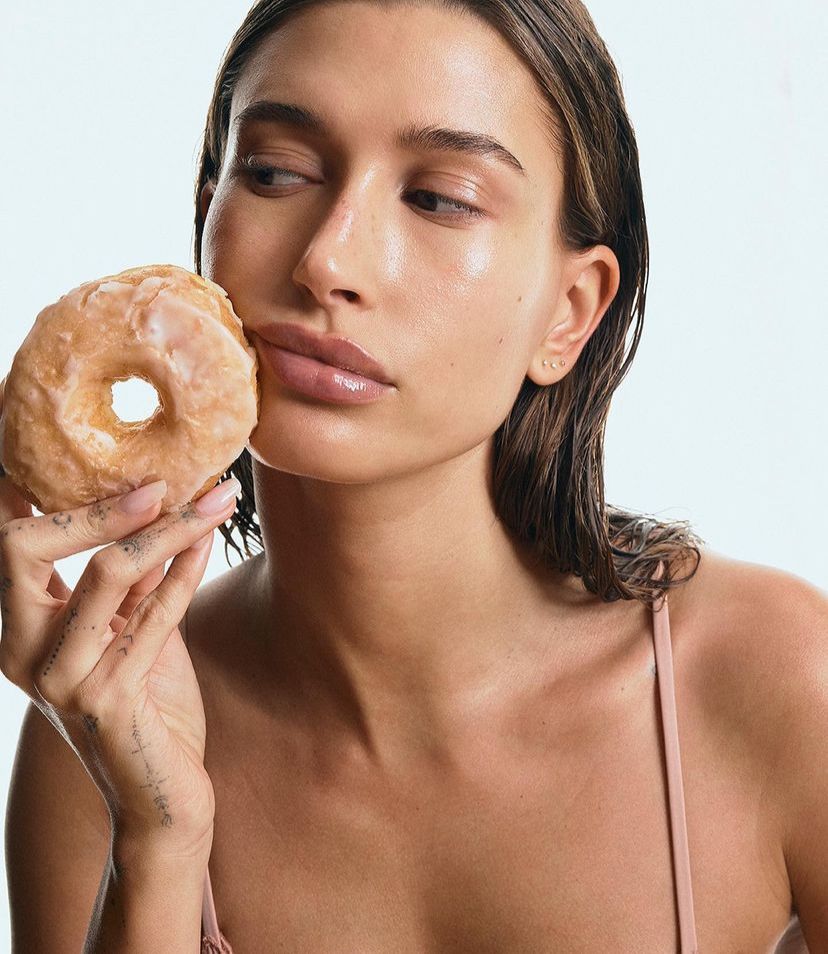 Saiba como reproduzir a glazed donut nails, unha perolada de Hailey Bieber Imagem mostra Hailey Bieber posando um donuts em campanha promocional para a Rhode, sua marca de produtos de skincare.