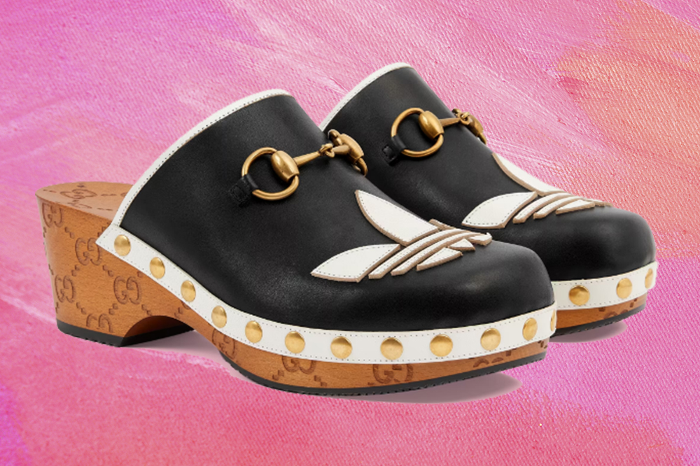 rihanna-clogs-gucci-adidas-polemica-anos-2010 Montagem em fundo rosa de sapato clogs preto e branco com detalhes em dourado da coleção da Adidas em parceria com a Gucci