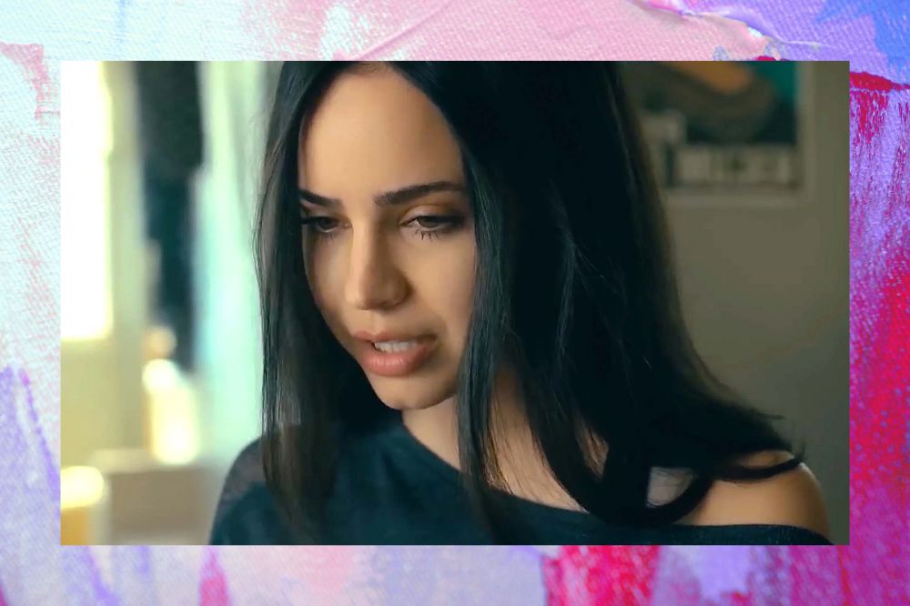 Sofia Carson olhando para baixo com blusa azul escura