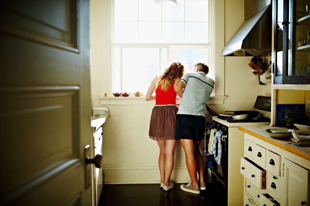 Casal de costas, apoiado na janela da cozinha, pensativos, como se estivessem cansados um do outro