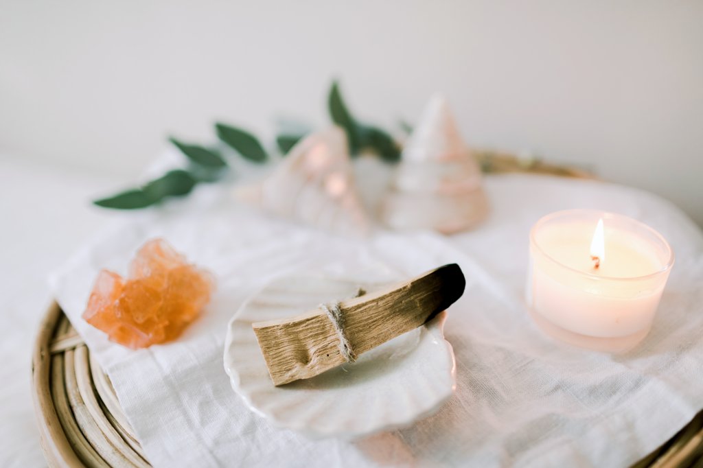 Objetos de limpeza espiritual, como palo santo, velas e cristais. Eles estãi sobre uma mesa branca