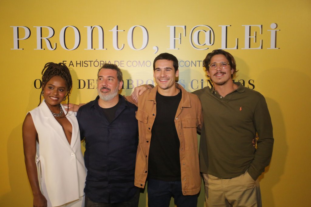 Elenco e diretor posando em frente à backdrop do filme