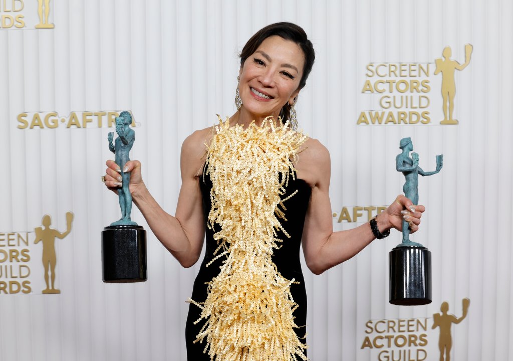 Michelle Yeoh no SAG Awards; ela está sorrindo enquanto posa para foto segurando dois troféus da premiação, um em cada mão