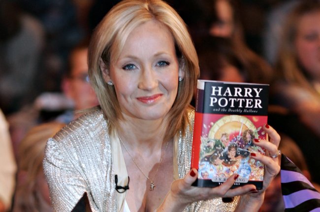 Não participar do boicote a Hogwarts Legacy te faz uma pessoa transfóbica? JK Rowling segurando um livro de Harry Potter. Ela é uma mulher branca, loira e alta