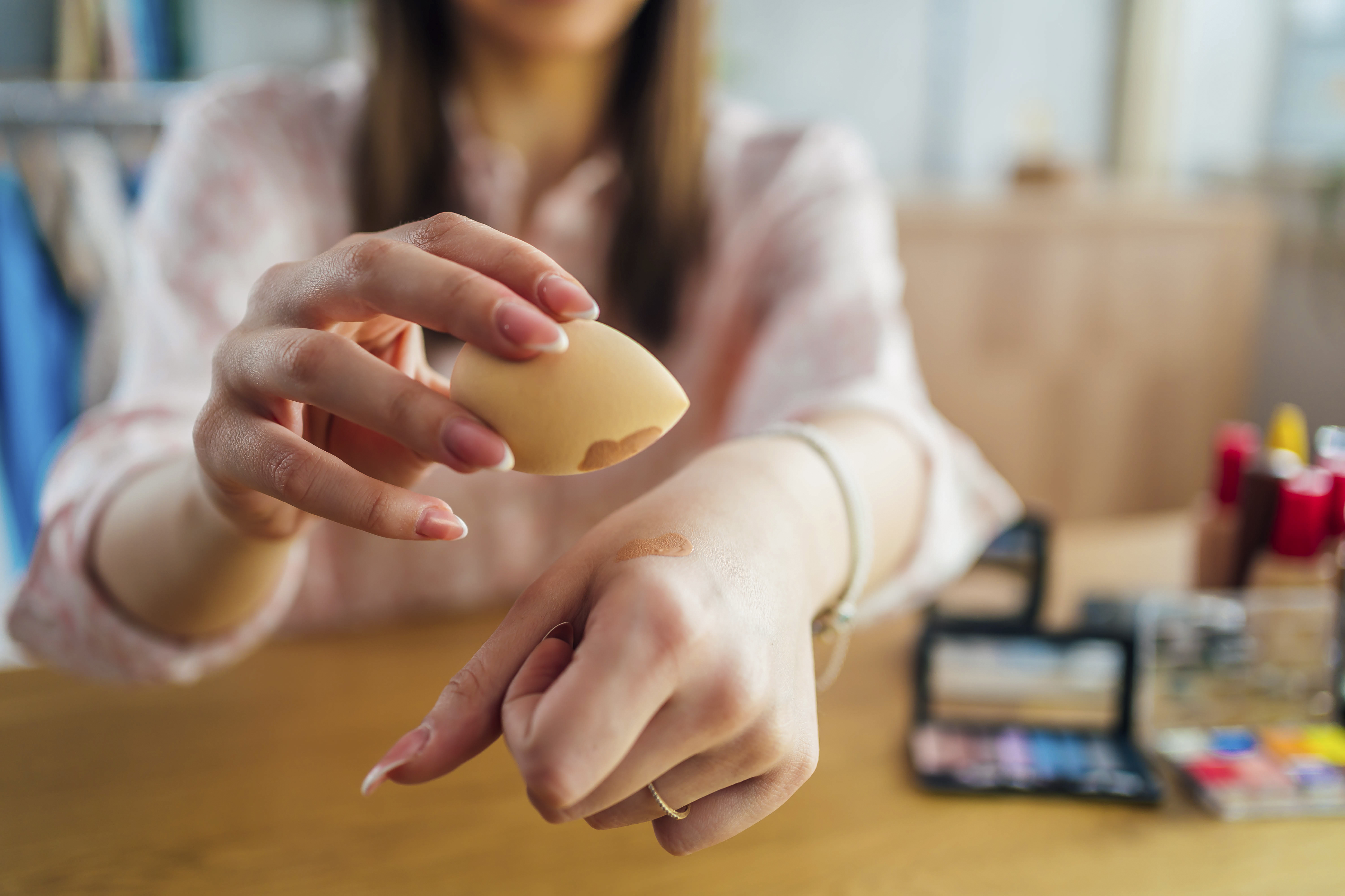 Mulher segurando uma esponjinha de maquiagem com base em uma das mãos