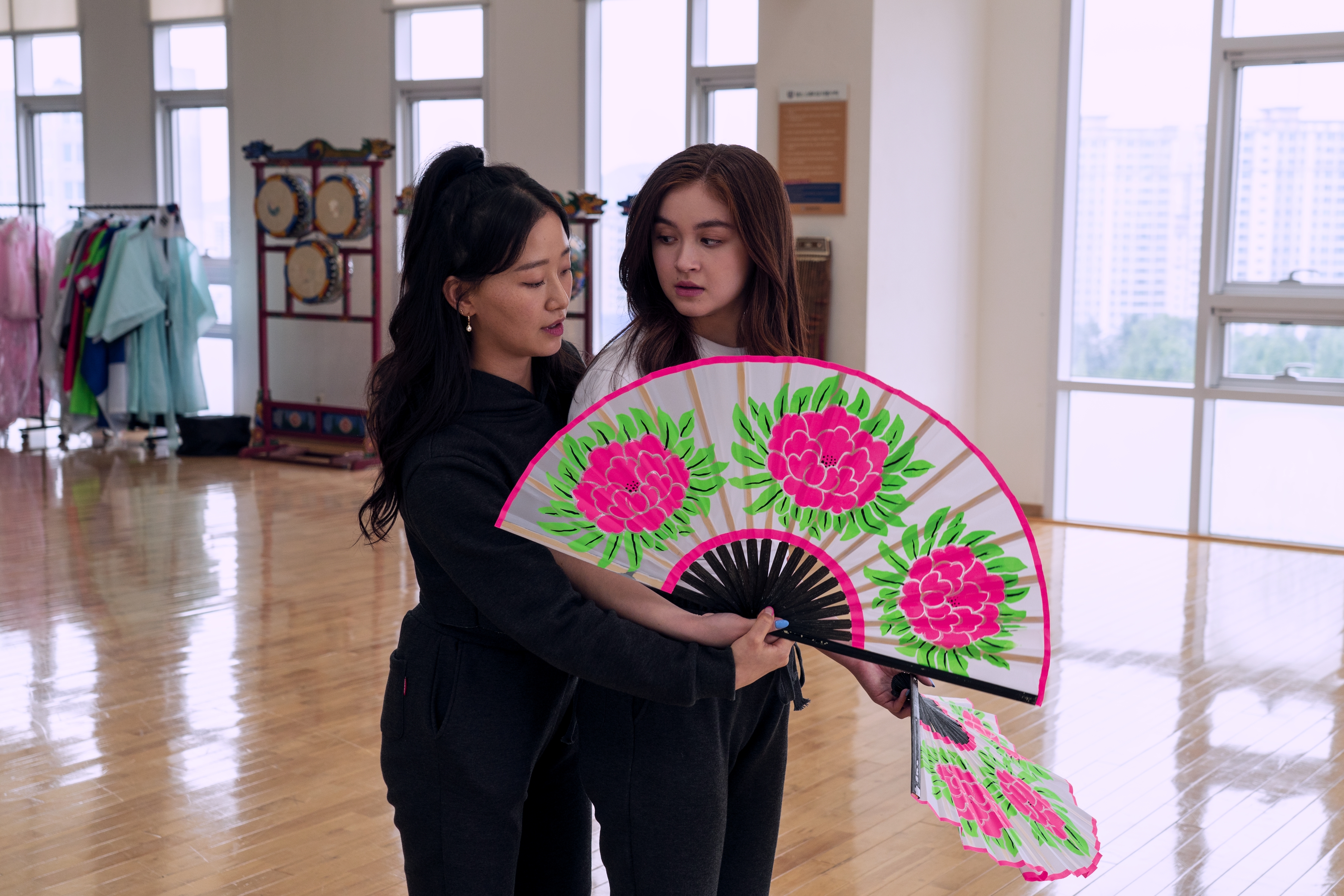 XO_109_Unit_00449RC Gia Kim como Yuri e Anna Cathcart como Kitty Song Covey em Com Carinho, Kitty; elas estão dançando com um leque; Yuri está atrás de Kitty olhando para o leque enquanto ela olha para Yuri