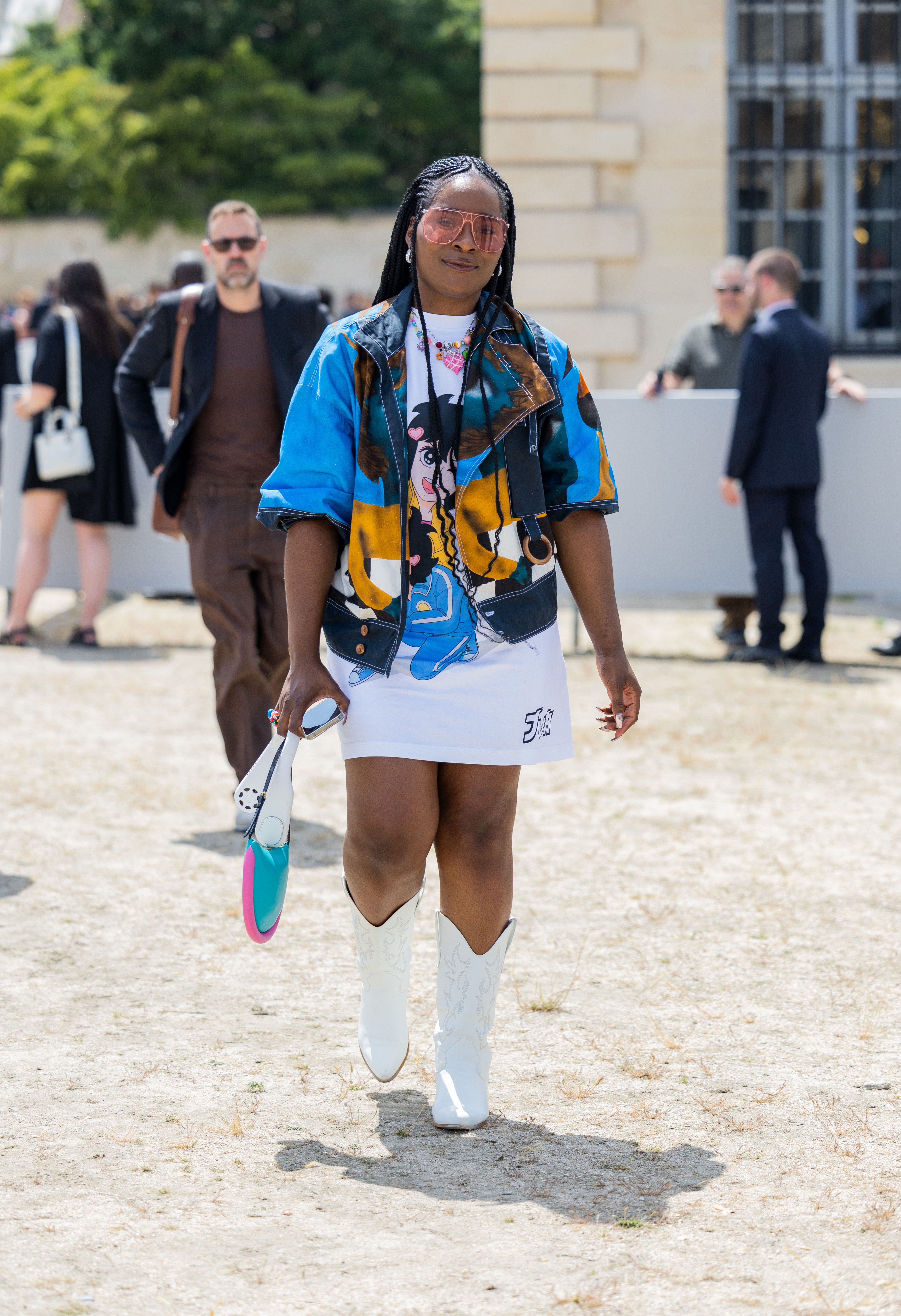 Look no street style da semana de moda masculina de primavera-verão 2024 em Paris. Mulher usando vestido branco estampado com camisa azul por cima e bota western branca