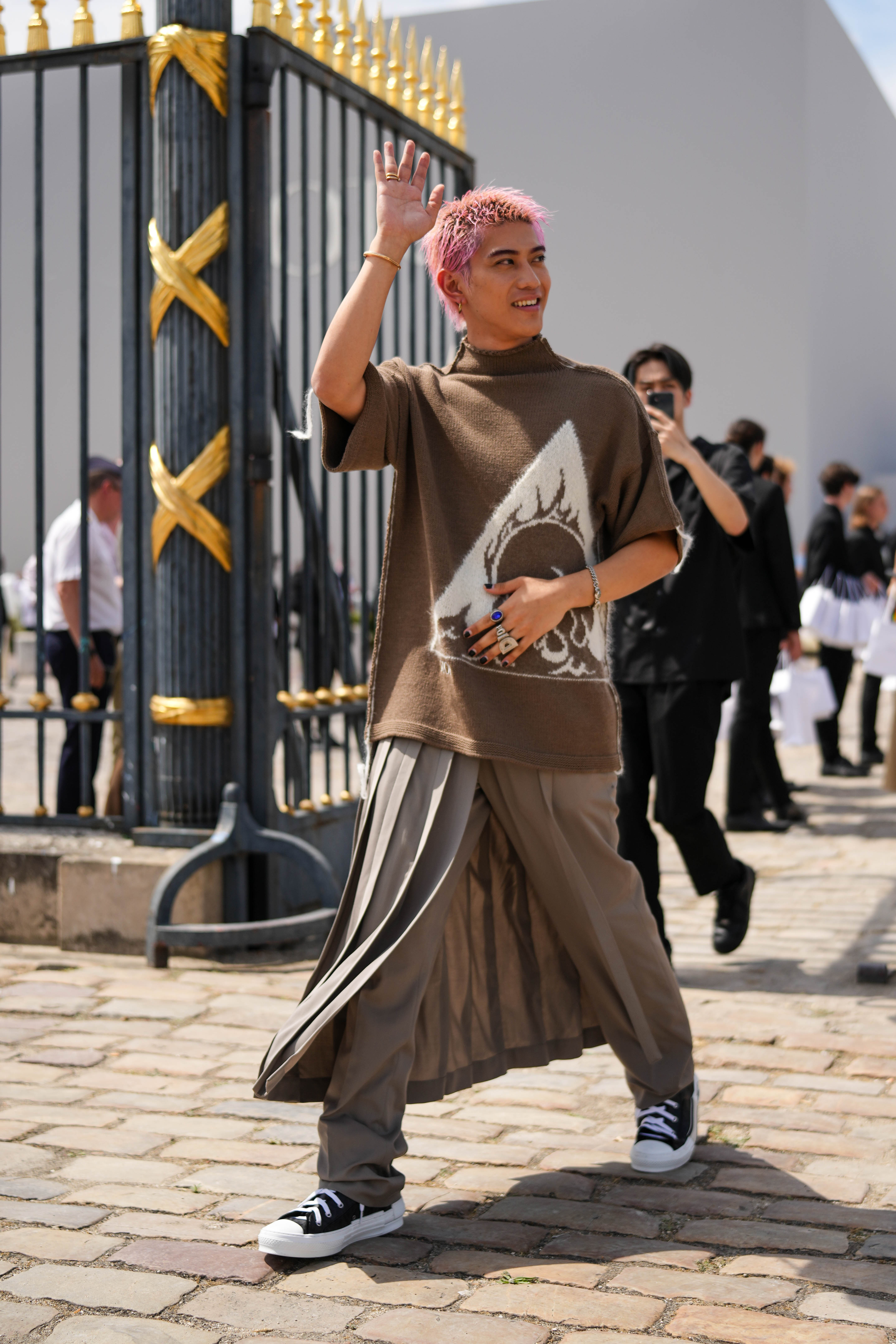 Look do Yamato no street style da semana de moda masculina de primavera-verão 2024 em Paris. Ele usa blusa de tricô marrom, calça em tom parecido com saia plissada por cima e tênis