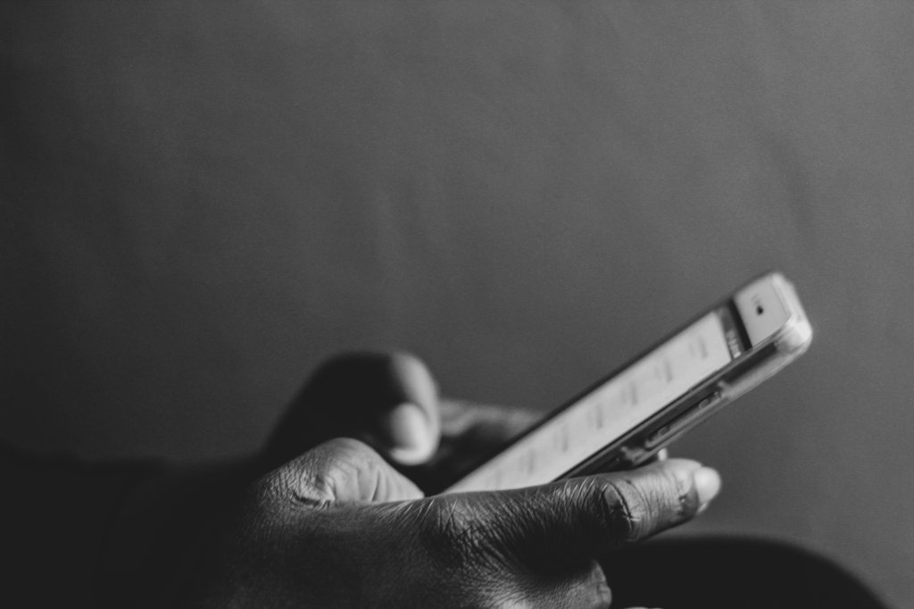 Na imagem branca e preta, aparece duas mãos digitando em um celular