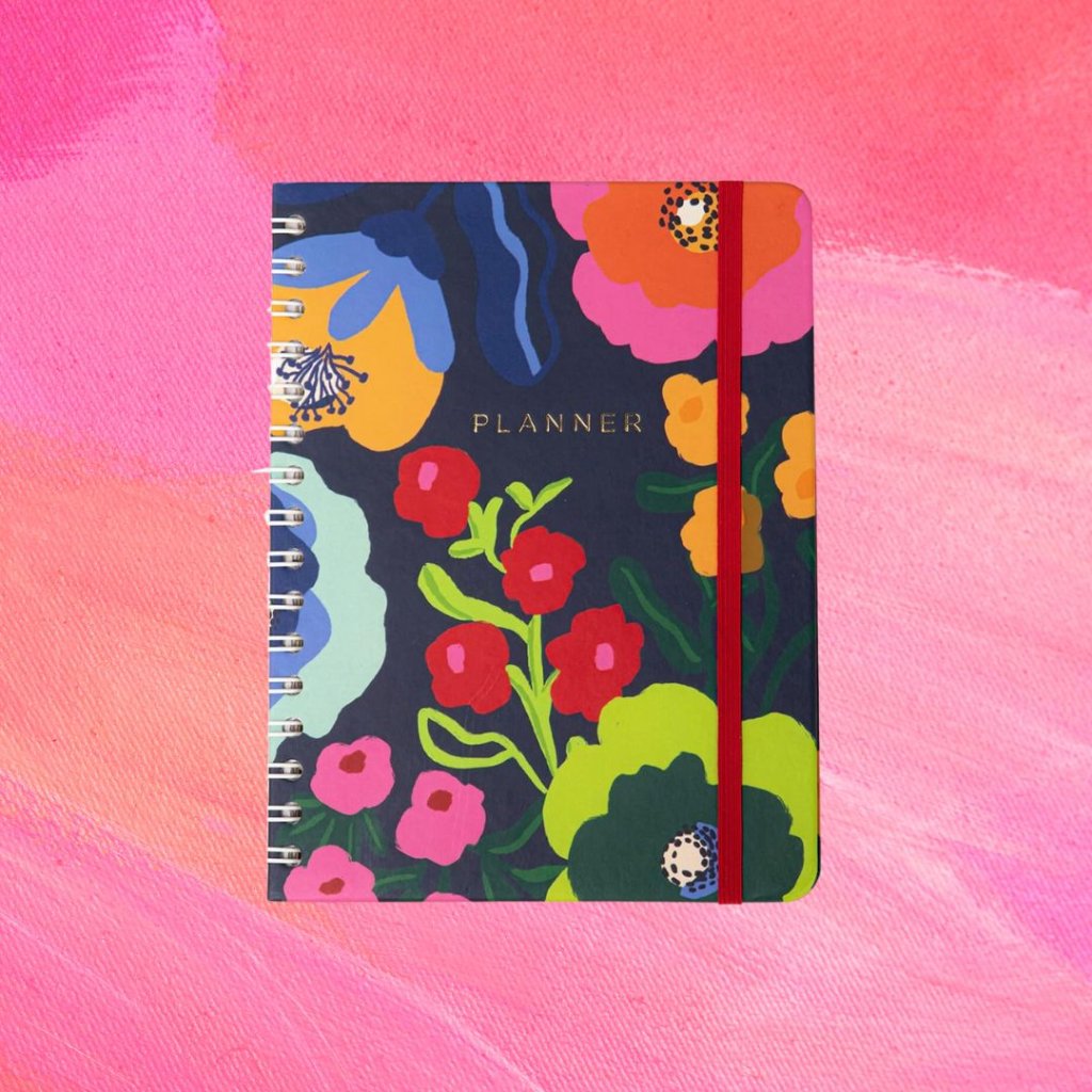 Planner florido em diferentes cores; o fundo é uma textura em tons de rosa e branco