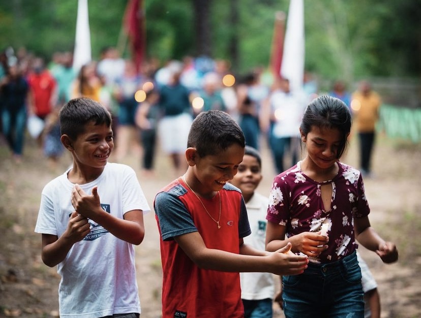 Na imagem aparecem quatro crianças. Eles estão sorrindo e segurando cada um uma vela