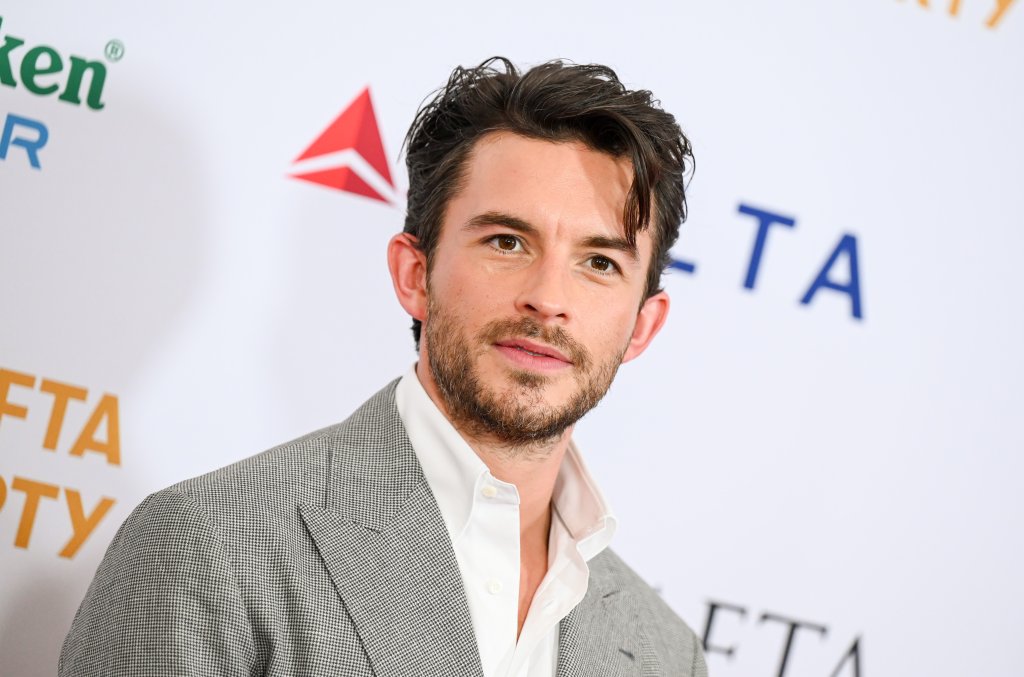 Jonathan Bailey posando para foto com expressão neutra; ele usa um terno cinza com camisa branca