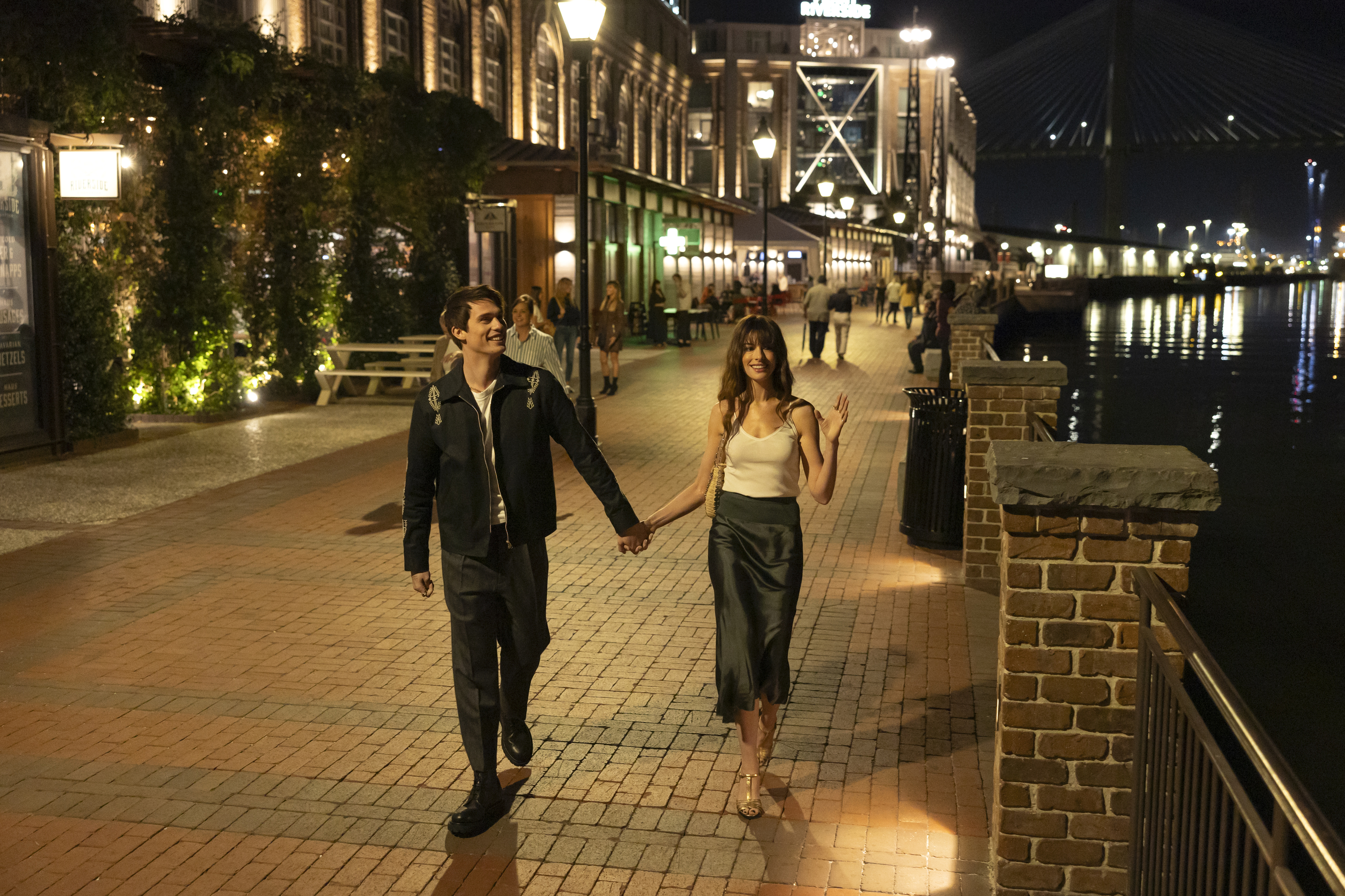 The Idea of You Nicholas Galitzine e Anne Hathaway em cena de Uma Ideia de Você; eles estão andando de mãos dadas pela rua durante a noite