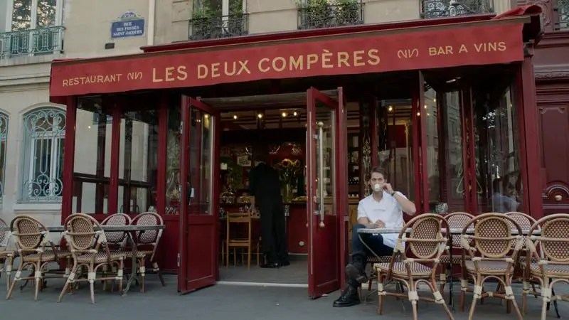 Cena de Emily em Paris, com o personagem Gabriel sentado em uma mesa de seus restaurante.