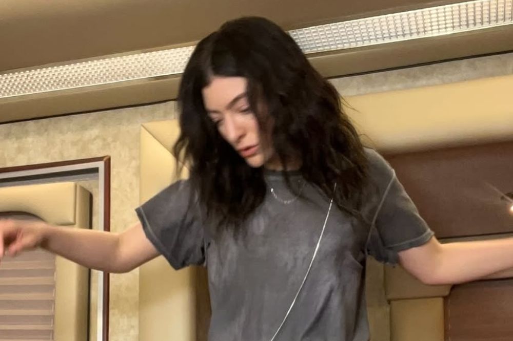 Lorde usando camiseta cinza e com os braços abertos em foto
