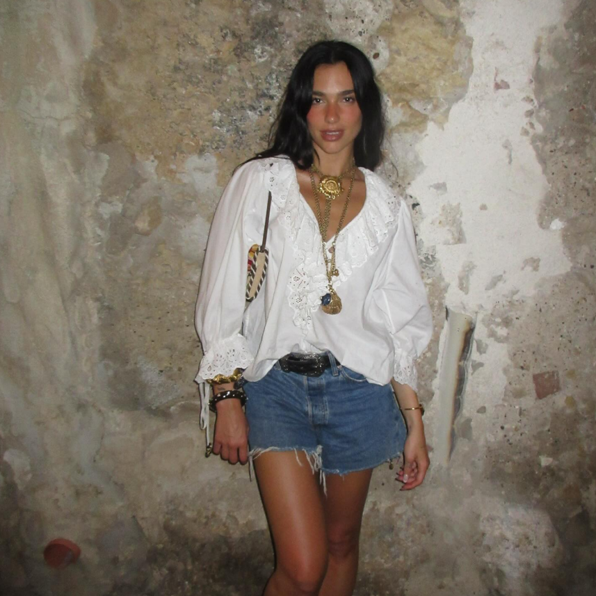 look-boho-dua-lipa-short-jeans Dua Lipa usando look boho com short jeans e camisa branca