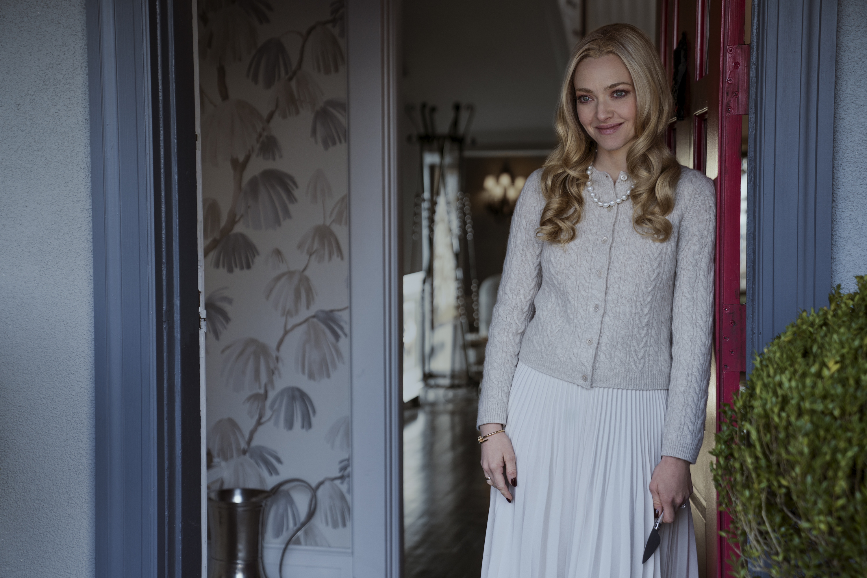 The Housemaid Amanda Seyfried usa roupas claras e se apoia em batente de porta