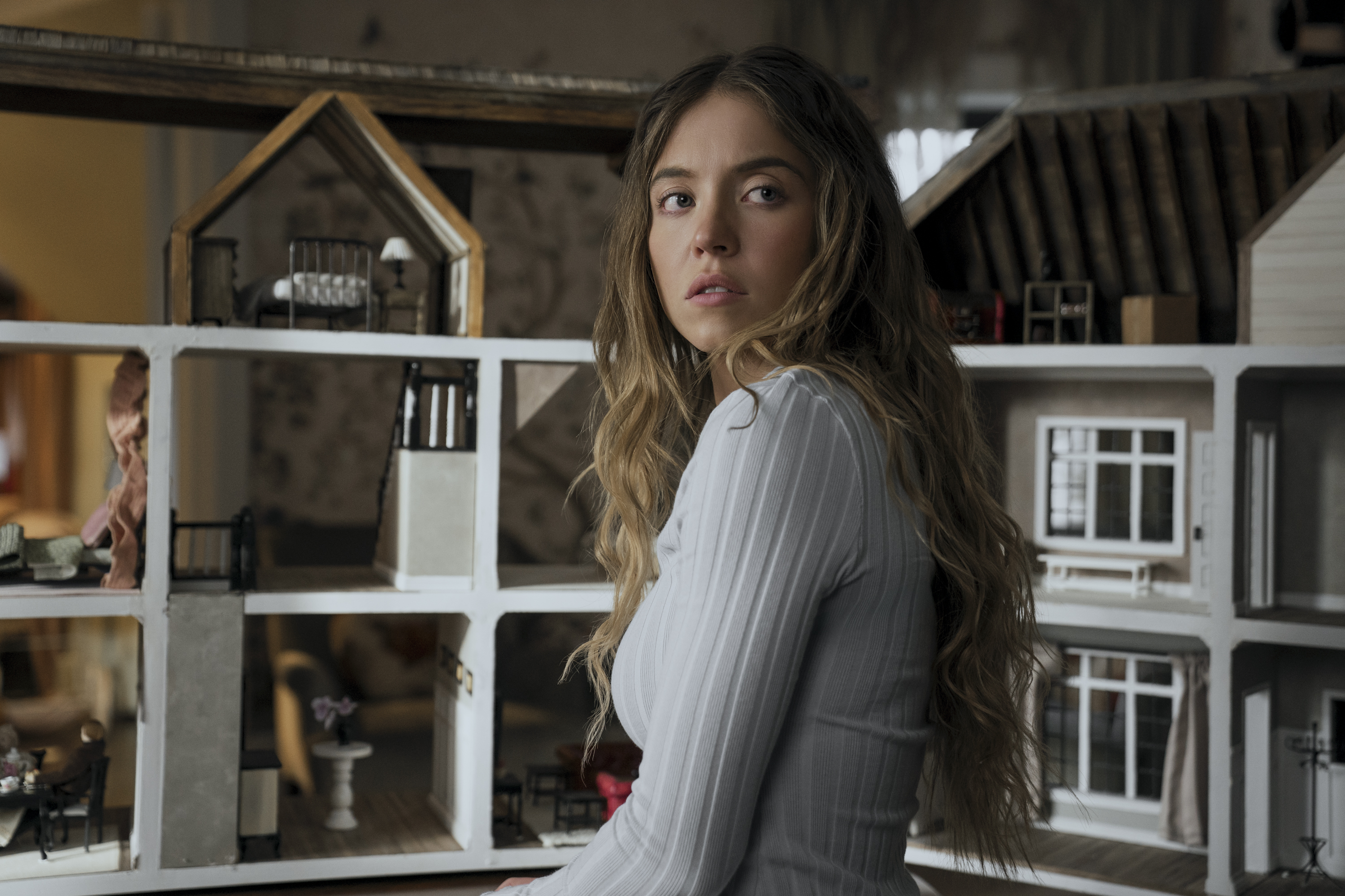 The Housemaid Sydney Sweeney olha para frente com casa de bonecas ao fundo