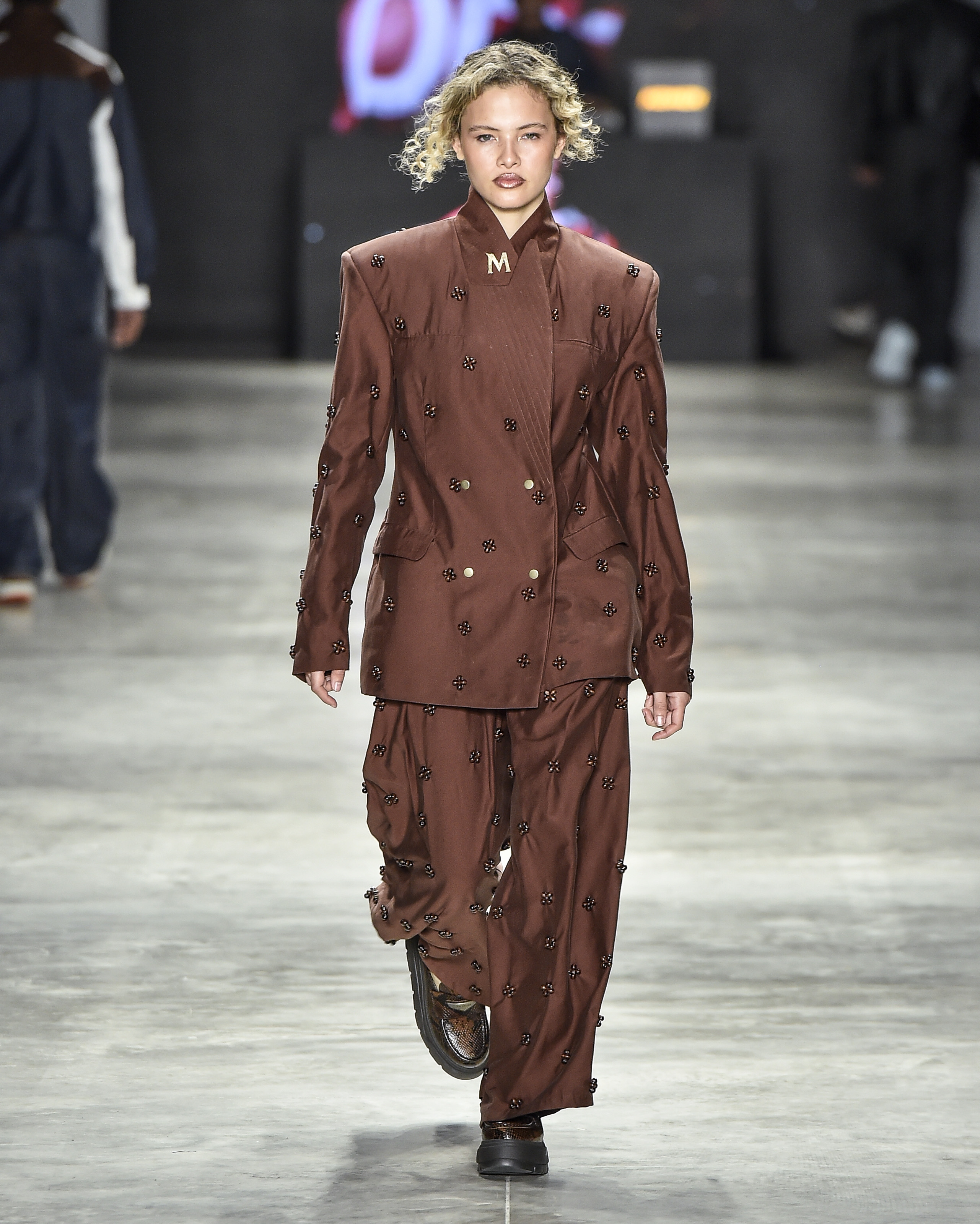 Modelo desfilando para a marca Dendezeiro com um conjunto de alfaiataria marrom