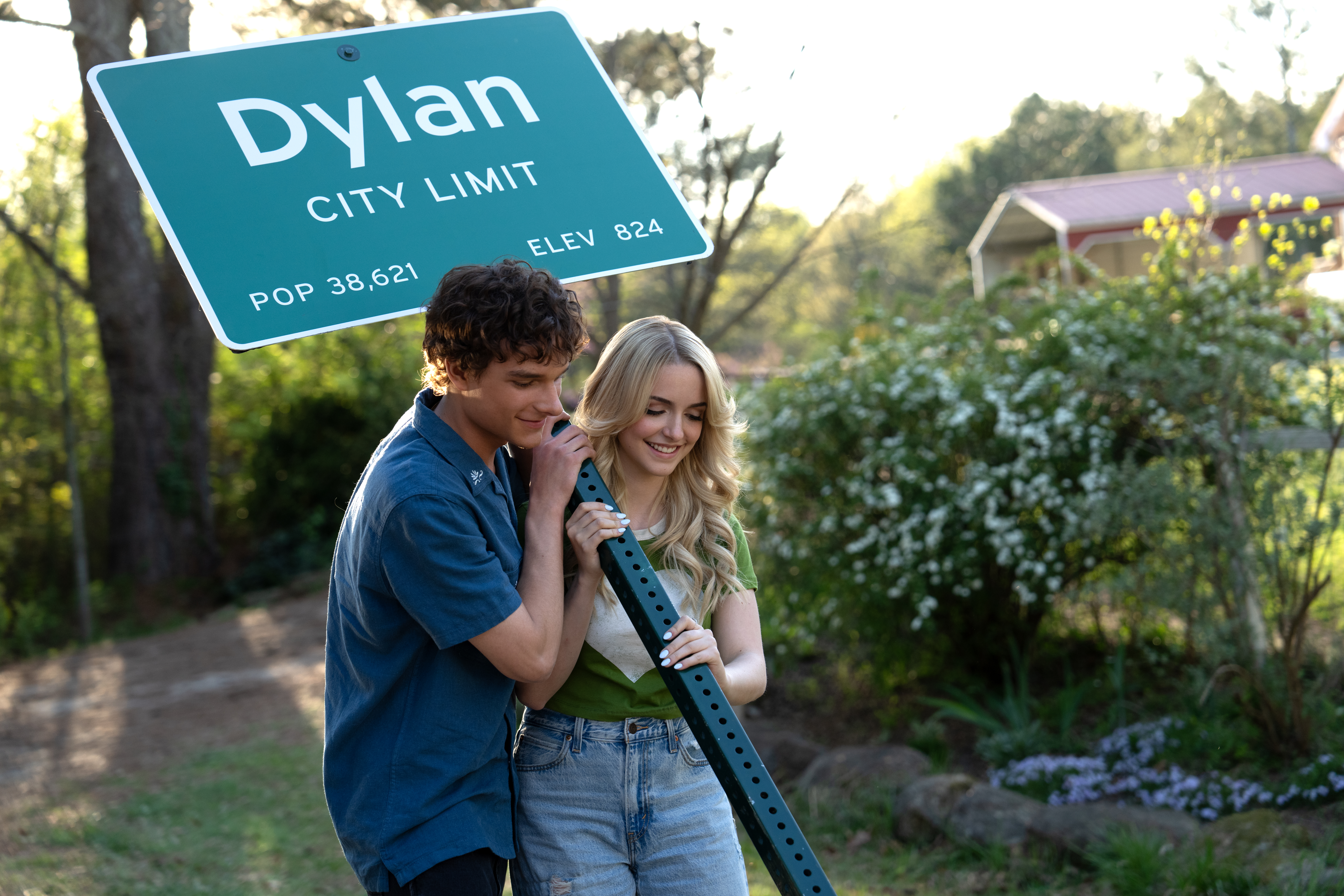 Mason Thames como Miller, e McKenna Grace como Clara segurando placa da cidade em cena de Se Não Fosse Você